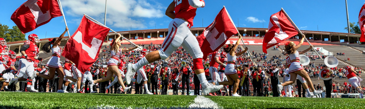 Cornell football player running onto field, cheerleaders and crowds