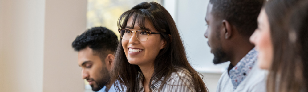Young woman with glasses smiling optimistically among diverse colleagues