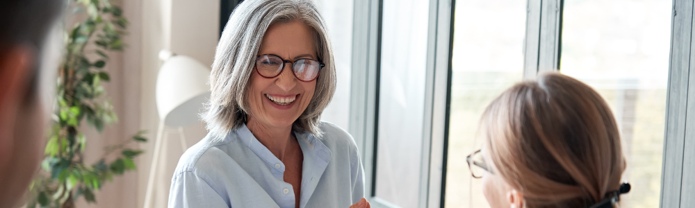 mature woman with glasses smiling at younger woman in office