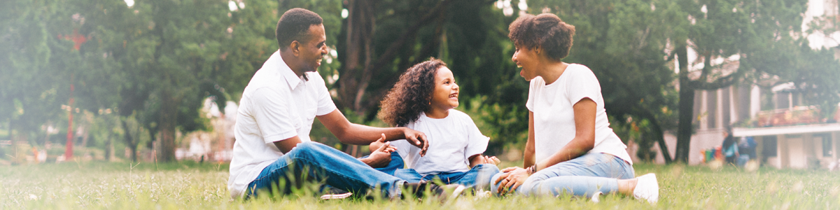 Black mom and dad with young daughter sitting in grass outdoors laughing