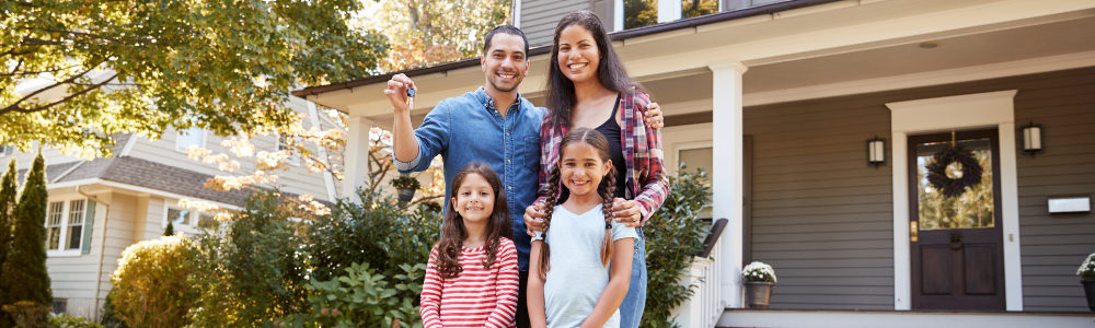 young latinx family with two daughters posing in front of lovely home with porch
