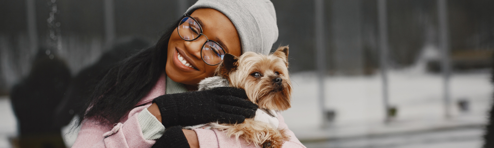 Black woman with glasses snuggling with puppy in winter