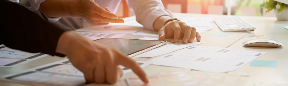 hands pointing to items on desk with lots of paper work