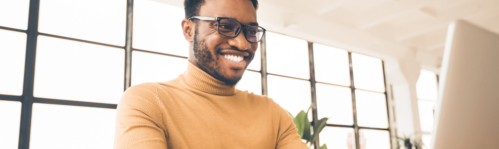 Black man looking down at laptop screen, smiling