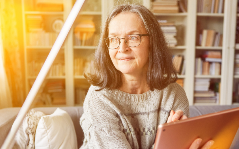 mature woman thinking with smile, sitting on couch with laptop