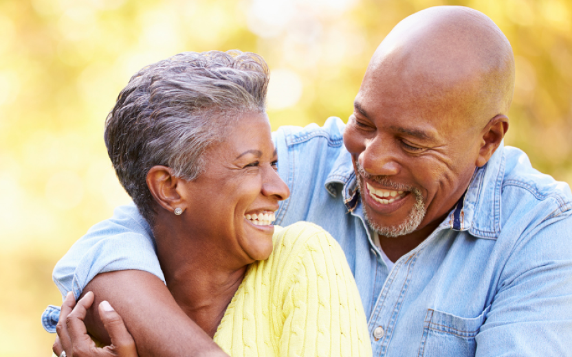 mature Black man and woman outdoors cuddling in golden light