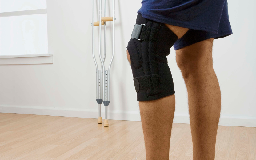 legs of person wearing knee brace; crutches in background