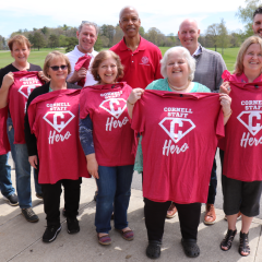 Group of colleagues posing outdoors holding red Cornell Heroes tshirts