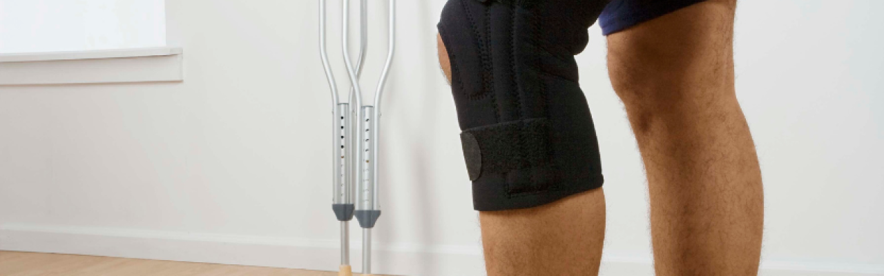 legs of person wearing knee brace; crutches in background